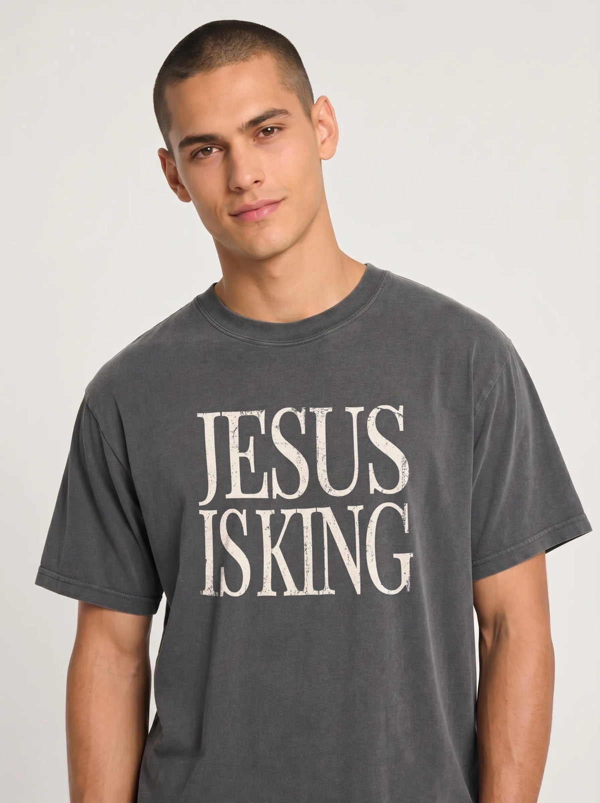 Person wearing a charcoal gray T-shirt with distressed cream text reading “Jesus Is King.”