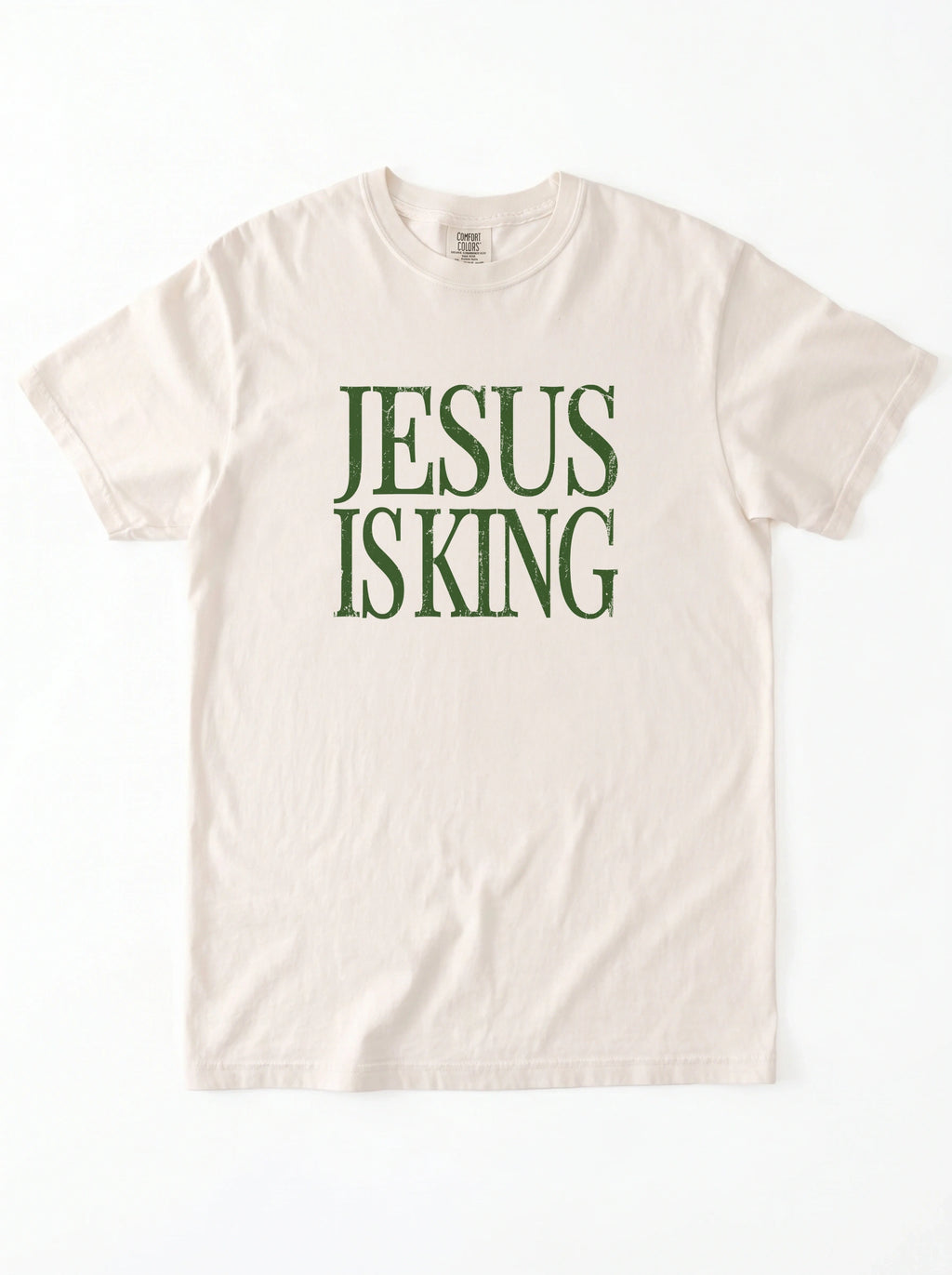 Cream T-shirt laid flat with distressed green text reading “Jesus Is King.”