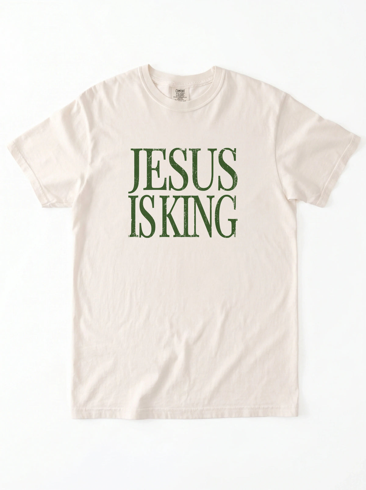 Cream T-shirt laid flat with distressed green text reading “Jesus Is King.”