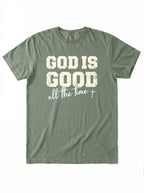 An olive green short-sleeve t-shirt with a distressed white graphic print on the front that reads 'GOD IS GOOD all the time +'.