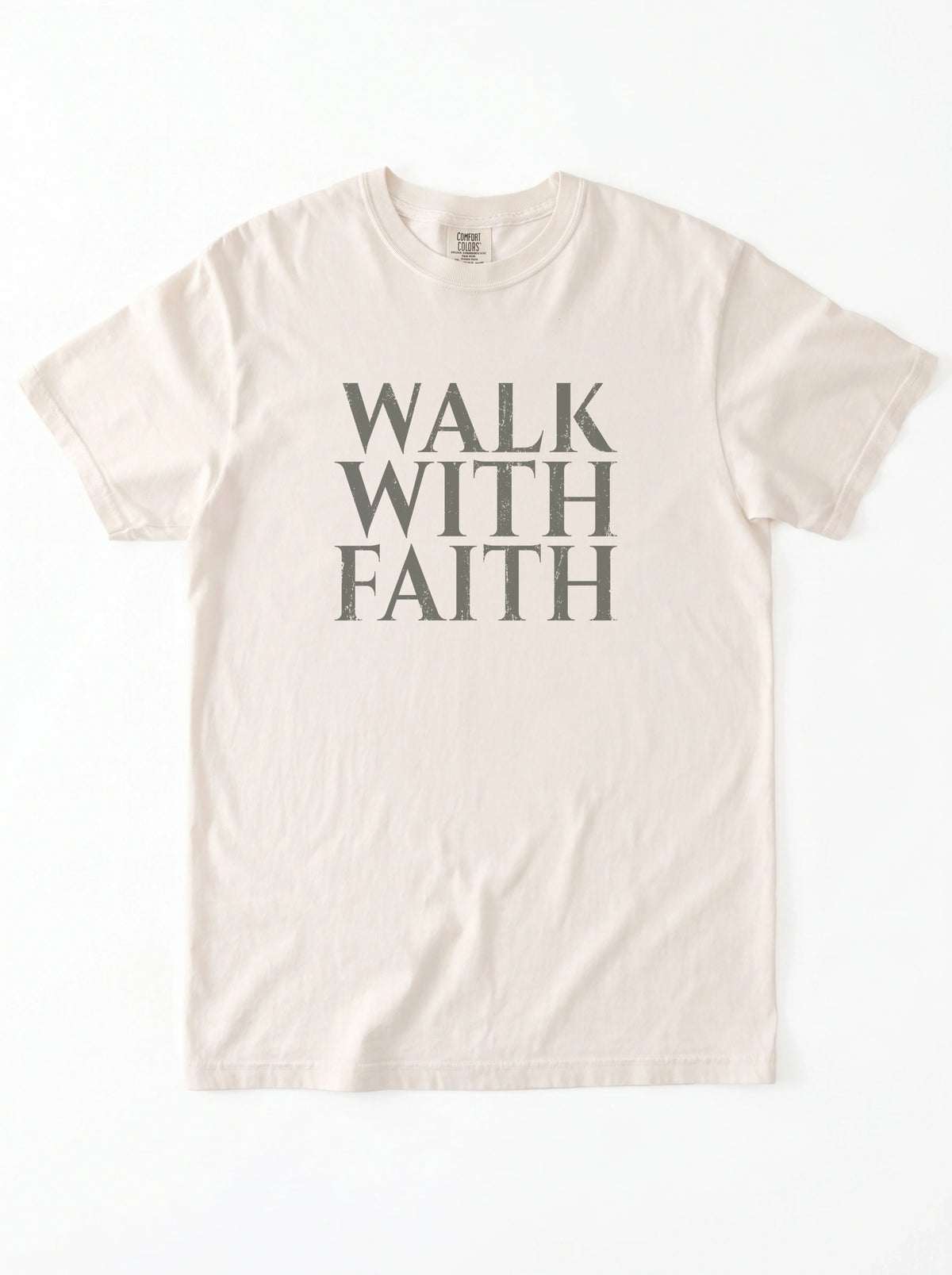 Cream T-shirt laid flat with distressed gray text reading “Walk With Faith.”