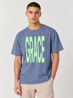 Person wearing a faded blue T-shirt with large neon green text reading “GRACE.”