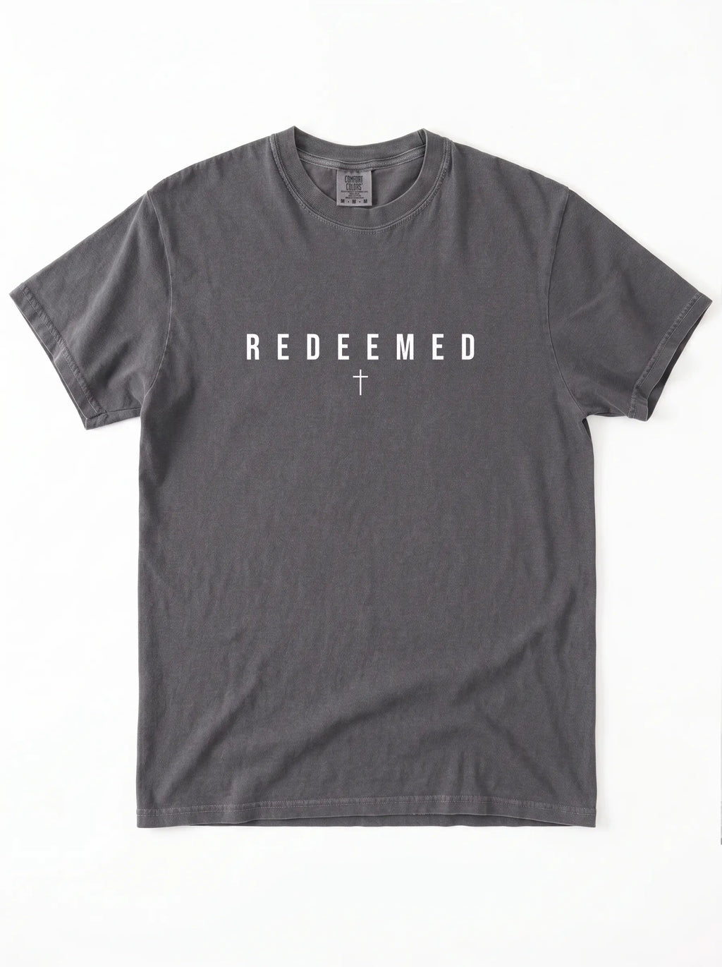 A dark gray crewneck t-shirt with the word 'REDEEMED' printed in white block letters across the chest, with a small white cross symbol underneath, displayed flat against a white background.