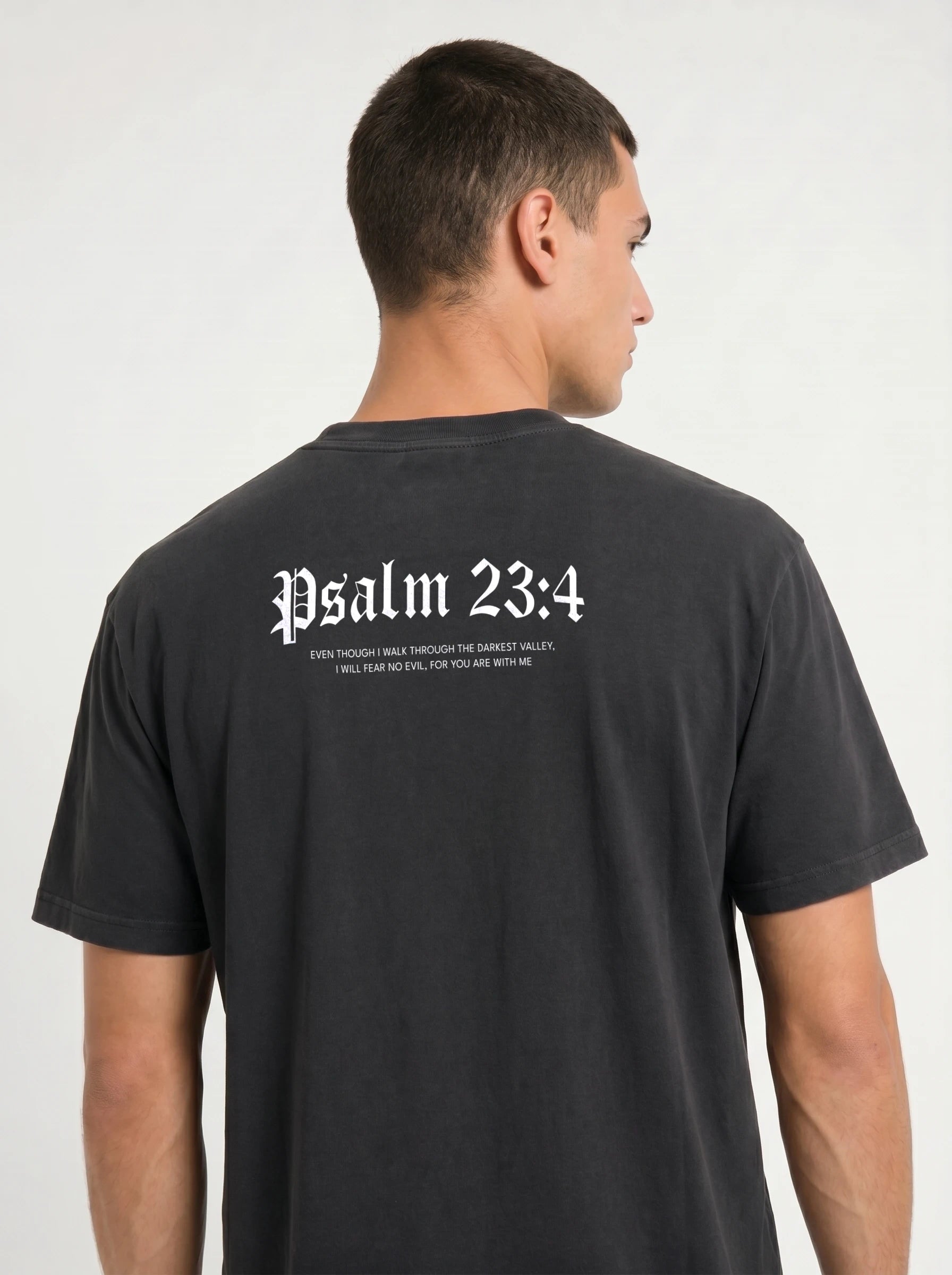 A man shown from the back wearing a black t-shirt with 'Psalm 23:4' printed in white Gothic lettering across the upper back.
