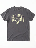 Flat lay view of a charcoal short-sleeve t-shirt on a white background, featuring the distressed yellow text "GOD OVER ALL THINGS" and a dove graphic on the chest.