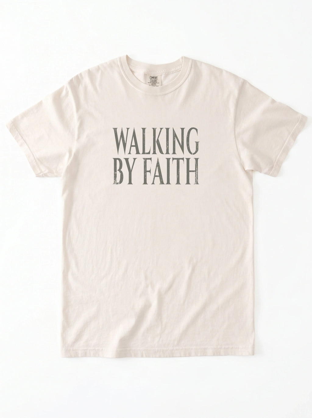 Cream T-shirt laid flat with distressed gray text reading “Walking By Faith.”