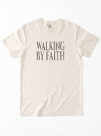 Cream T-shirt laid flat with distressed gray text reading “Walking By Faith.”