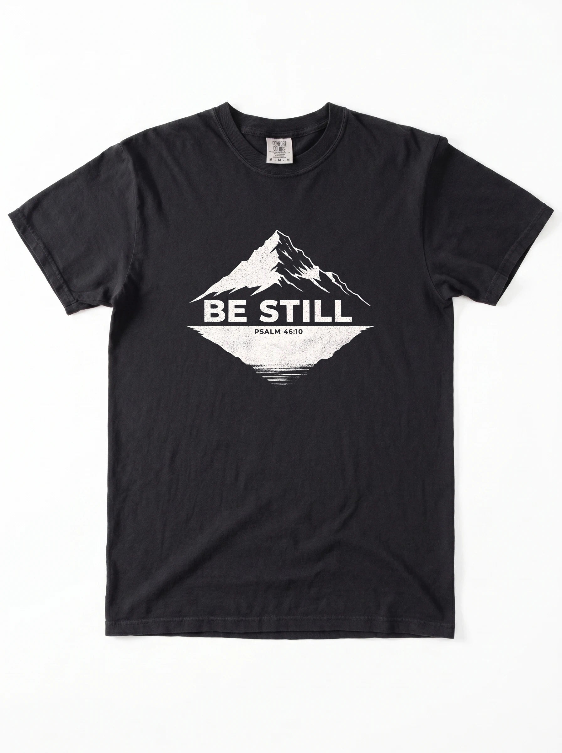 A black short-sleeve crewneck t-shirt with a white graphic on the chest showing a mountain peak, a lake reflection, and the text 'BE STILL' and 'PSALM 46:10'.