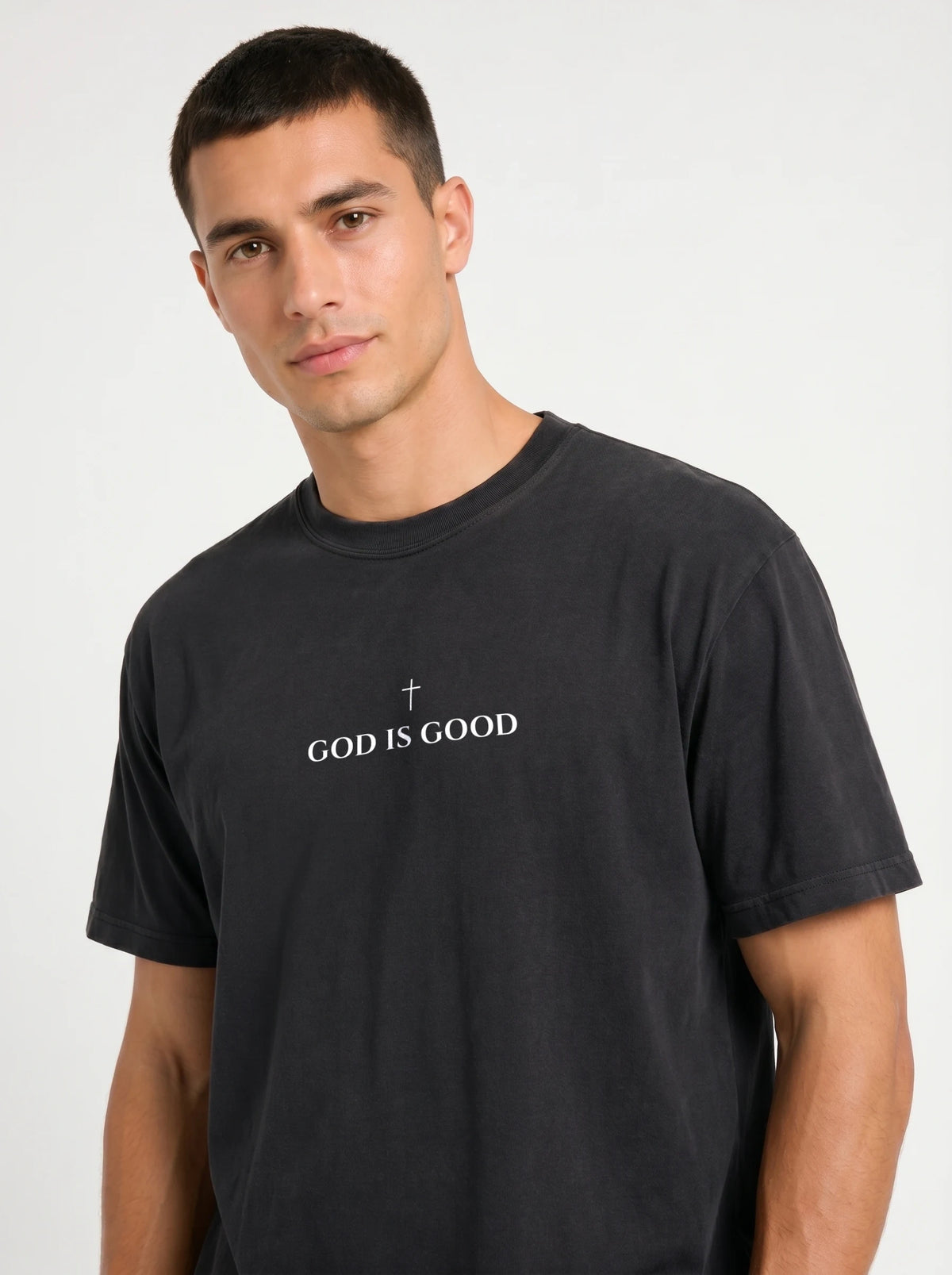 Person wearing a black T-shirt with a small cross above the text “God Is Good.”
