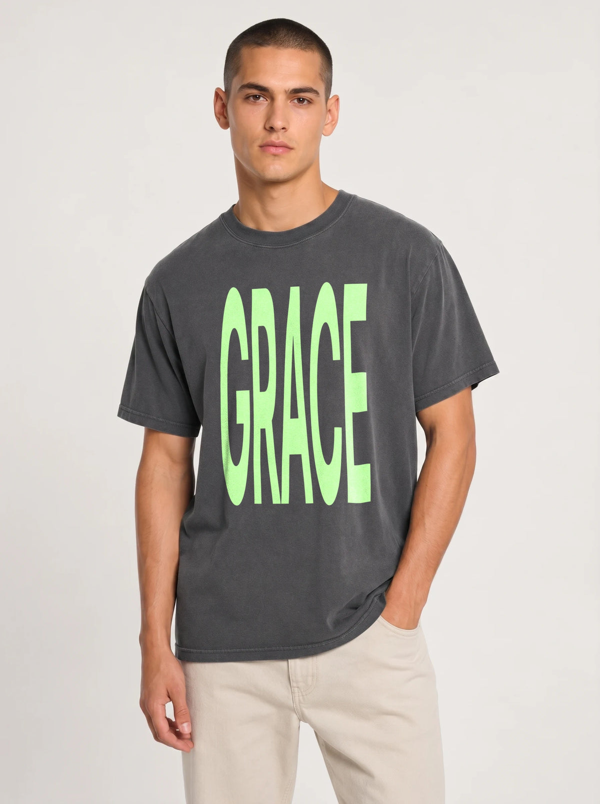 Person wearing a faded charcoal T-shirt with large neon green text reading “GRACE.”