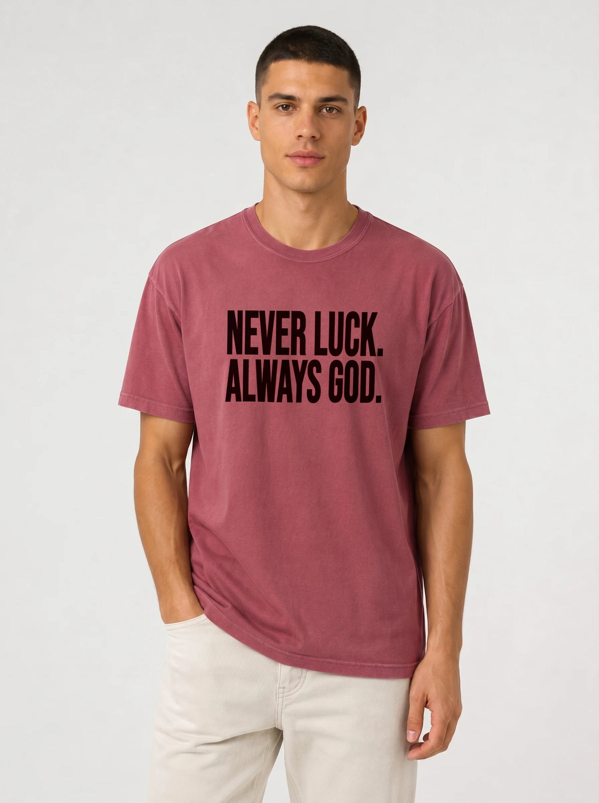 Person wearing a faded red T-shirt with black text reading “Never luck. Always God.”