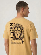 Person wearing a yellow T-shirt with a black lion illustration, cross, “1 John 4:4,” and the verse text, “You, dear children, are from God and have overcome them, because the one who is in you is greater than the one who is in the world.”