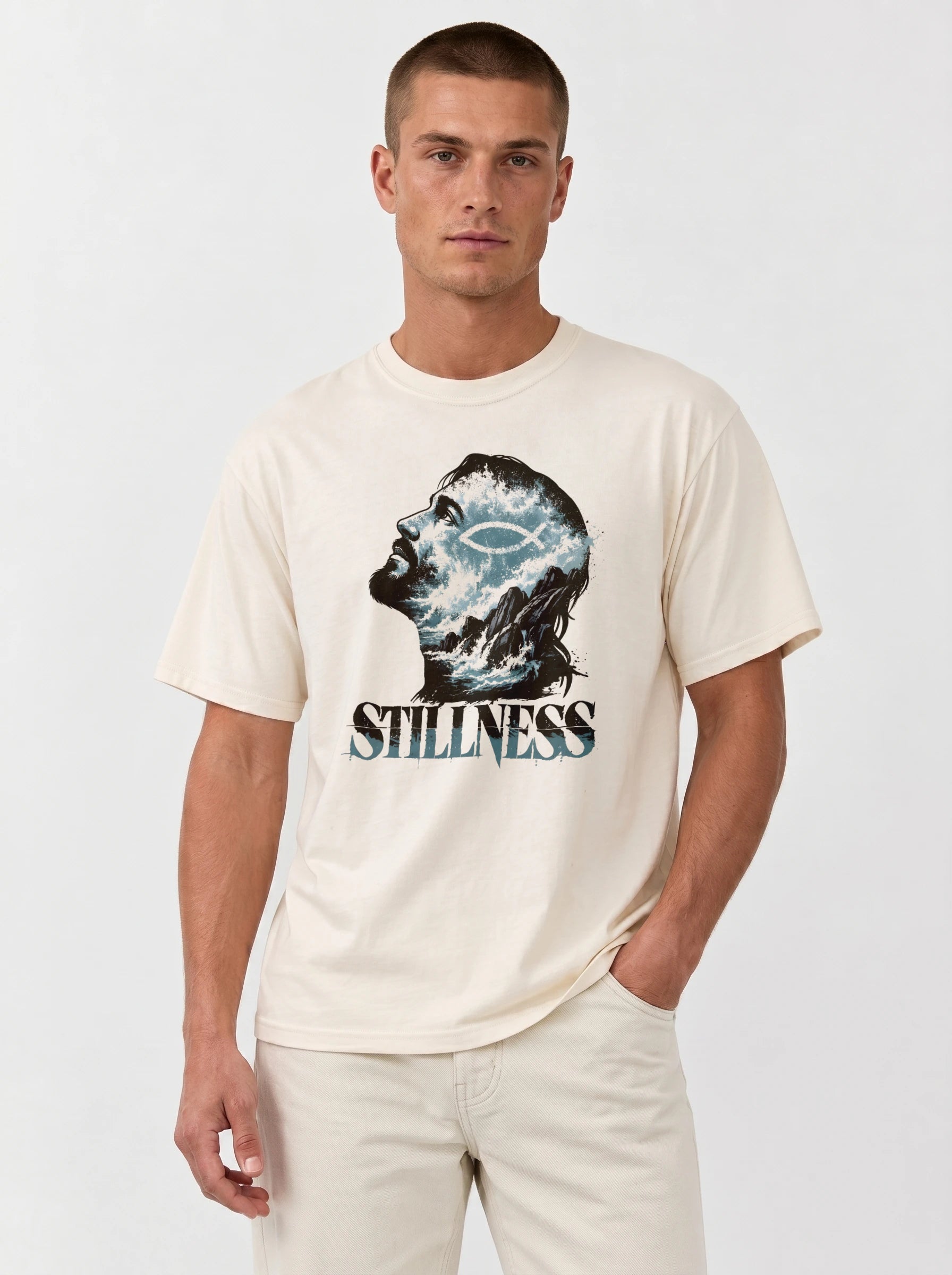A man wearing a cream-colored t-shirt with a graphic of a human head filled with water and a crescent moon, above the word 'STILLNESS'.