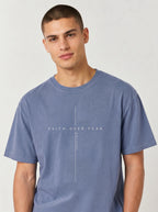 Person wearing a faded blue T-shirt with a minimalist cross design and the text “Faith Over Fear” and “Psalm 118:6.”