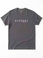 Flat lay of charcoal Comfort Colors 1717 Victory t-shirt with cross graphic and 1 Corinthians 15:57