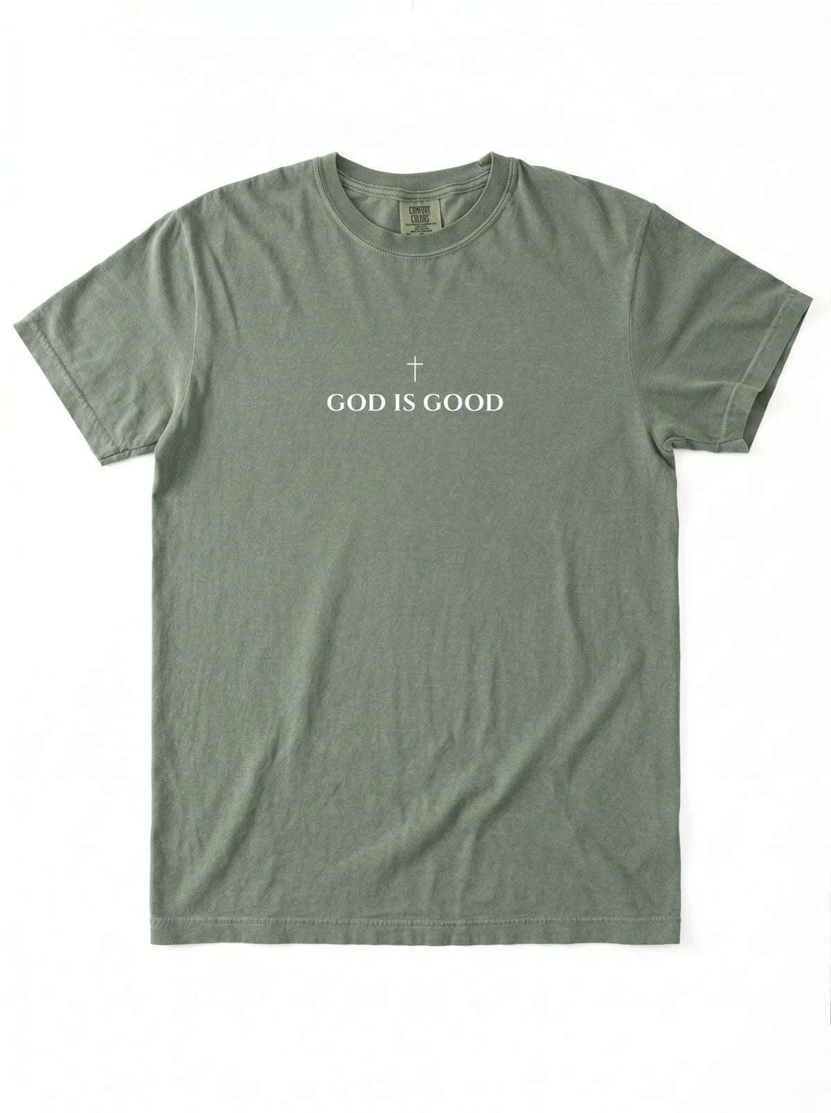 Muted green T-shirt laid flat with a small cross above the text “God Is Good.”