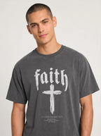 Person wearing a charcoal T-shirt with “faith,” a large cross, and the text “1 Corinthians 16:13 — Be watchful. Stand firm in the faith. Be strong.”