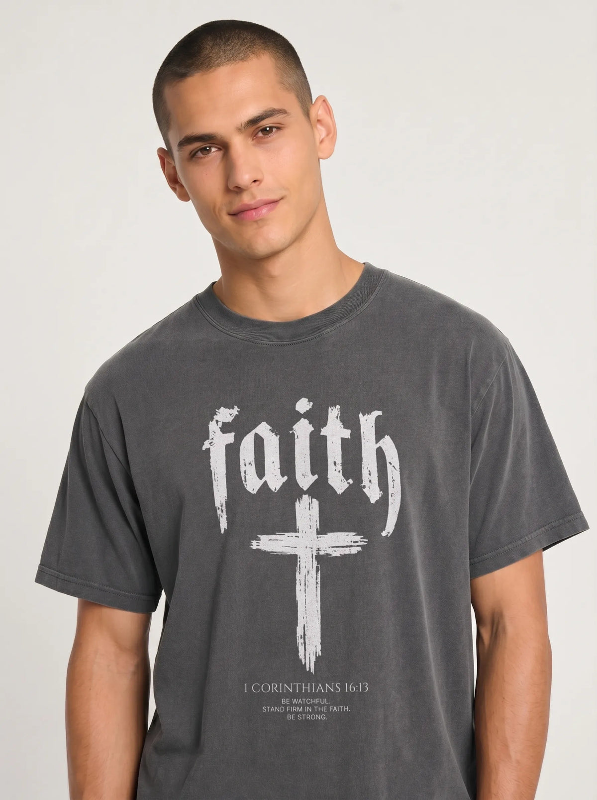 Person wearing a charcoal T-shirt with “faith,” a large cross, and the text “1 Corinthians 16:13 — Be watchful. Stand firm in the faith. Be strong.”