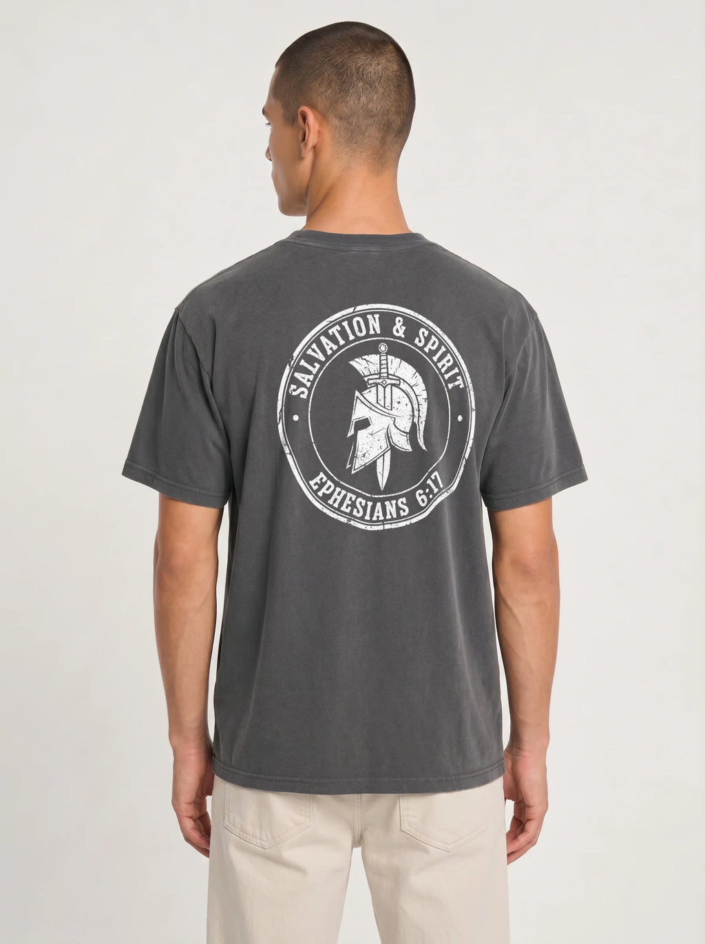 A man viewed from the back wearing a dark gray t-shirt with a white circular graphic on the back featuring a gladiator helmet and the text 'SALVATION & SPIRIT EPHESIANS 6:17'.
