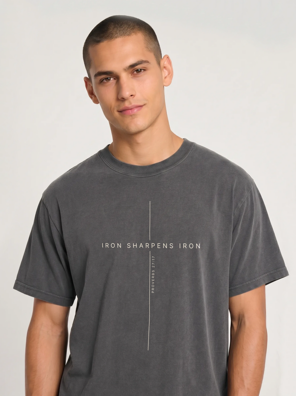 Medium shot of a male model wearing a vintage dark grey short-sleeve t-shirt with a white cross and "IRON SHARPENS IRON" text design.