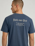 A man wearing a navy blue t-shirt, viewed from the back. The shirt features the text 'Faith over Fear' in a gothic font, followed by a bible verse from Psalms 118:6 in biege print.