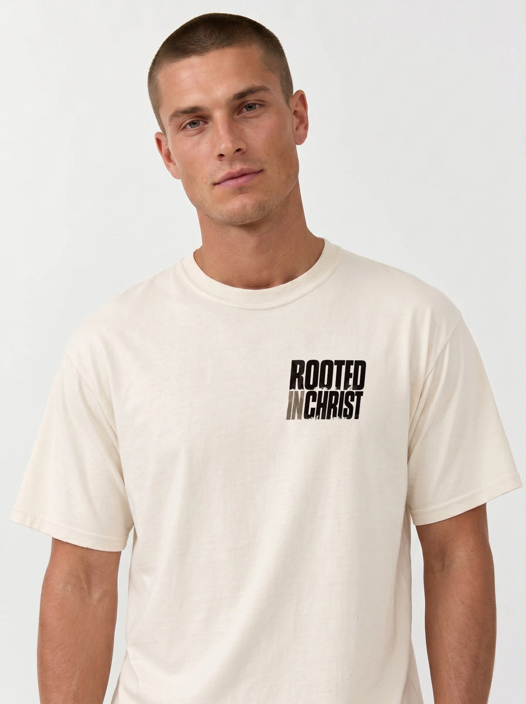 Person wearing a cream T-shirt with a distressed chest print reading “Rooted in Christ.”