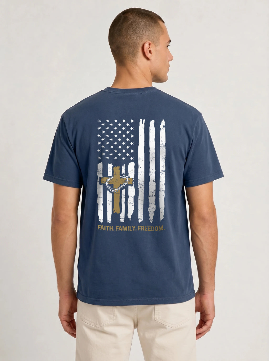 A man viewed from the back wearing a navy blue t-shirt with a distressed American flag graphic on the back, featuring a gold cross, stars, and the words 'FAITH, FAMILY, FREEDOM'.