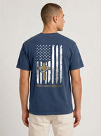 A man viewed from the back wearing a navy blue t-shirt with a distressed American flag graphic on the back, featuring a gold cross, stars, and the words 'FAITH, FAMILY, FREEDOM'.