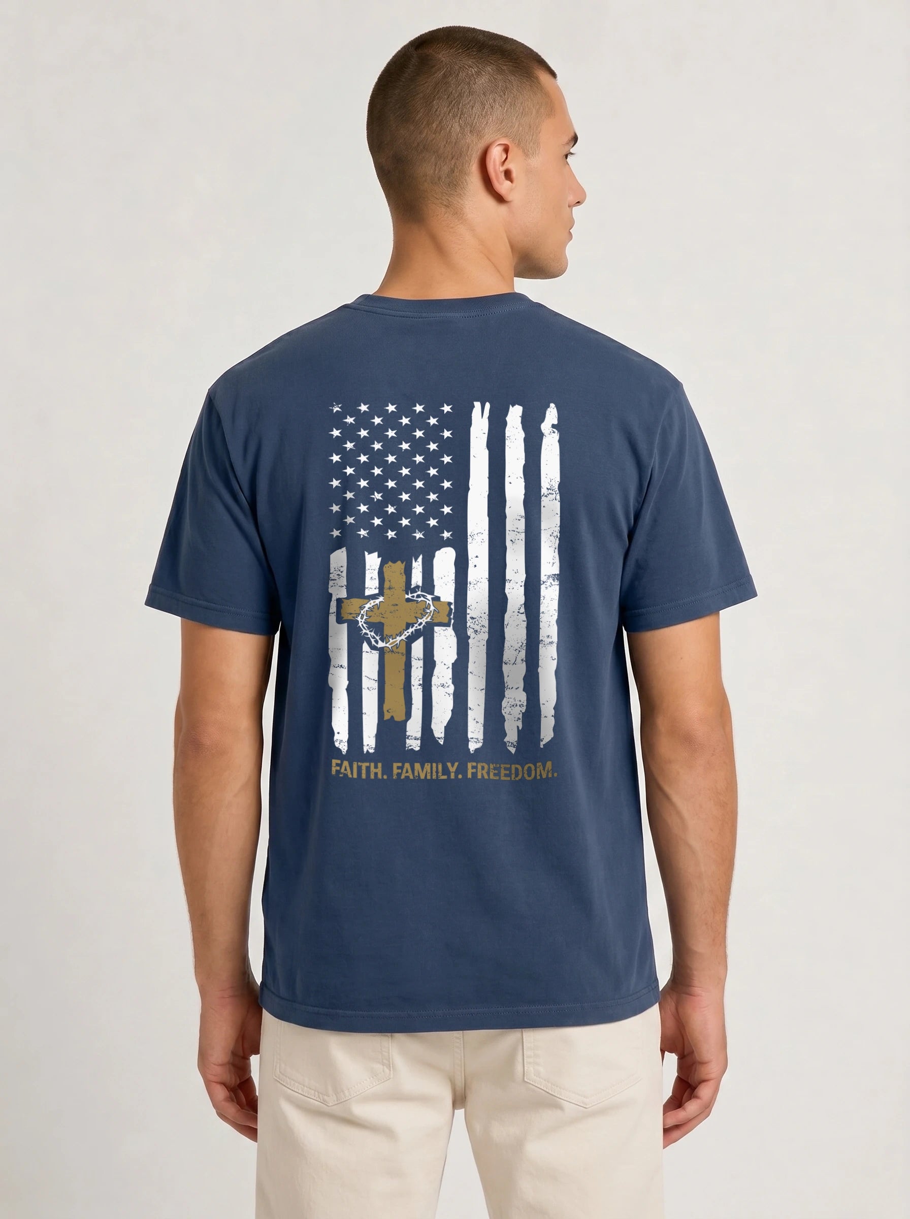 A man viewed from the back wearing a navy blue t-shirt with a distressed American flag graphic on the back, featuring a gold cross, stars, and the words 'FAITH, FAMILY, FREEDOM'.