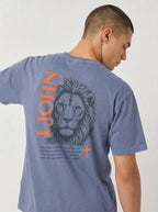 Person wearing a blue T-shirt with a dark lion illustration, orange “1 John 4:4” and cross, and the verse “You, dear children, are from God and have overcome them, because the one who is in you is greater than the one who is in the world.”