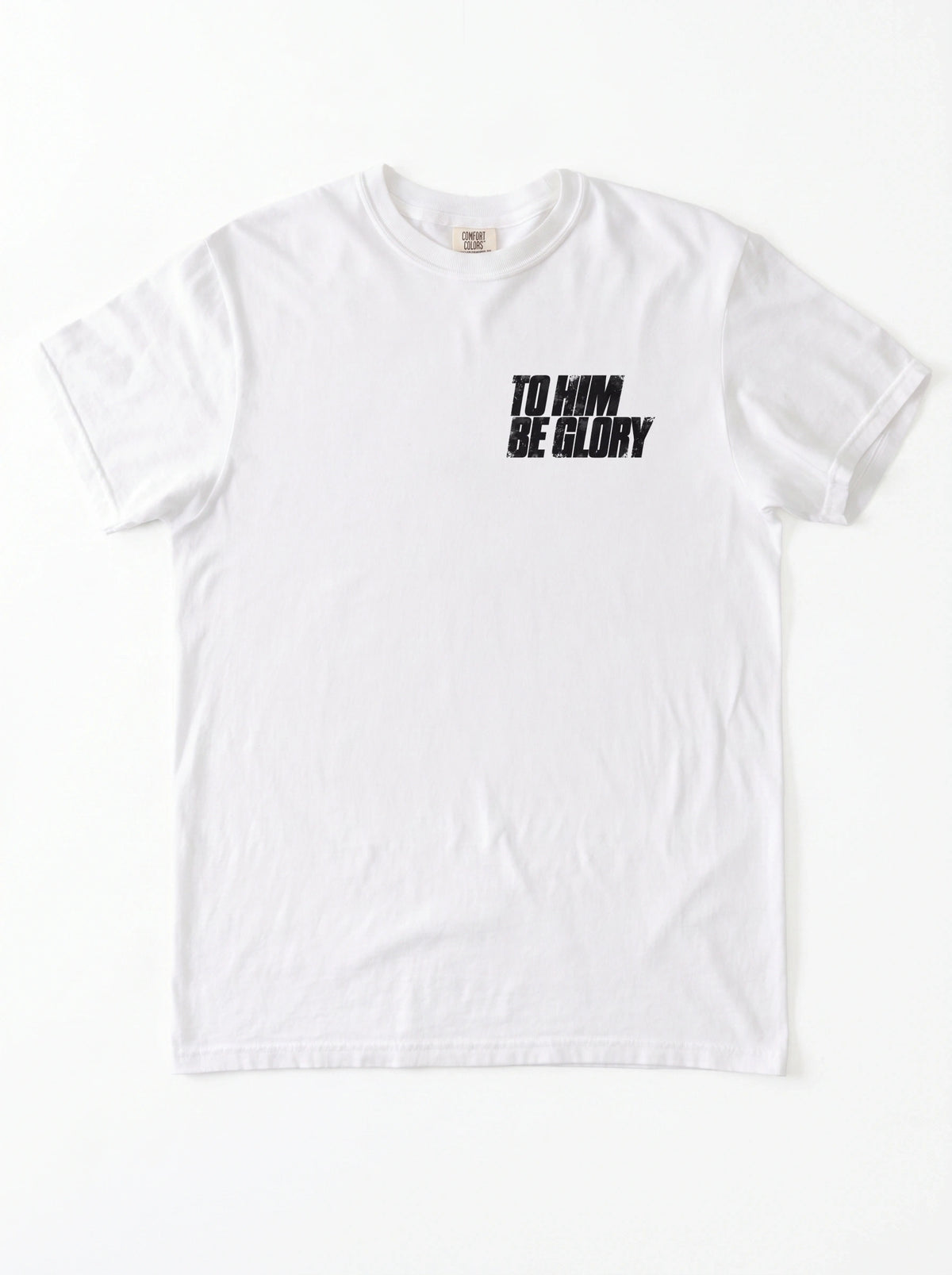White T-shirt laid flat with a distressed chest print reading “To Him Be Glory.”
