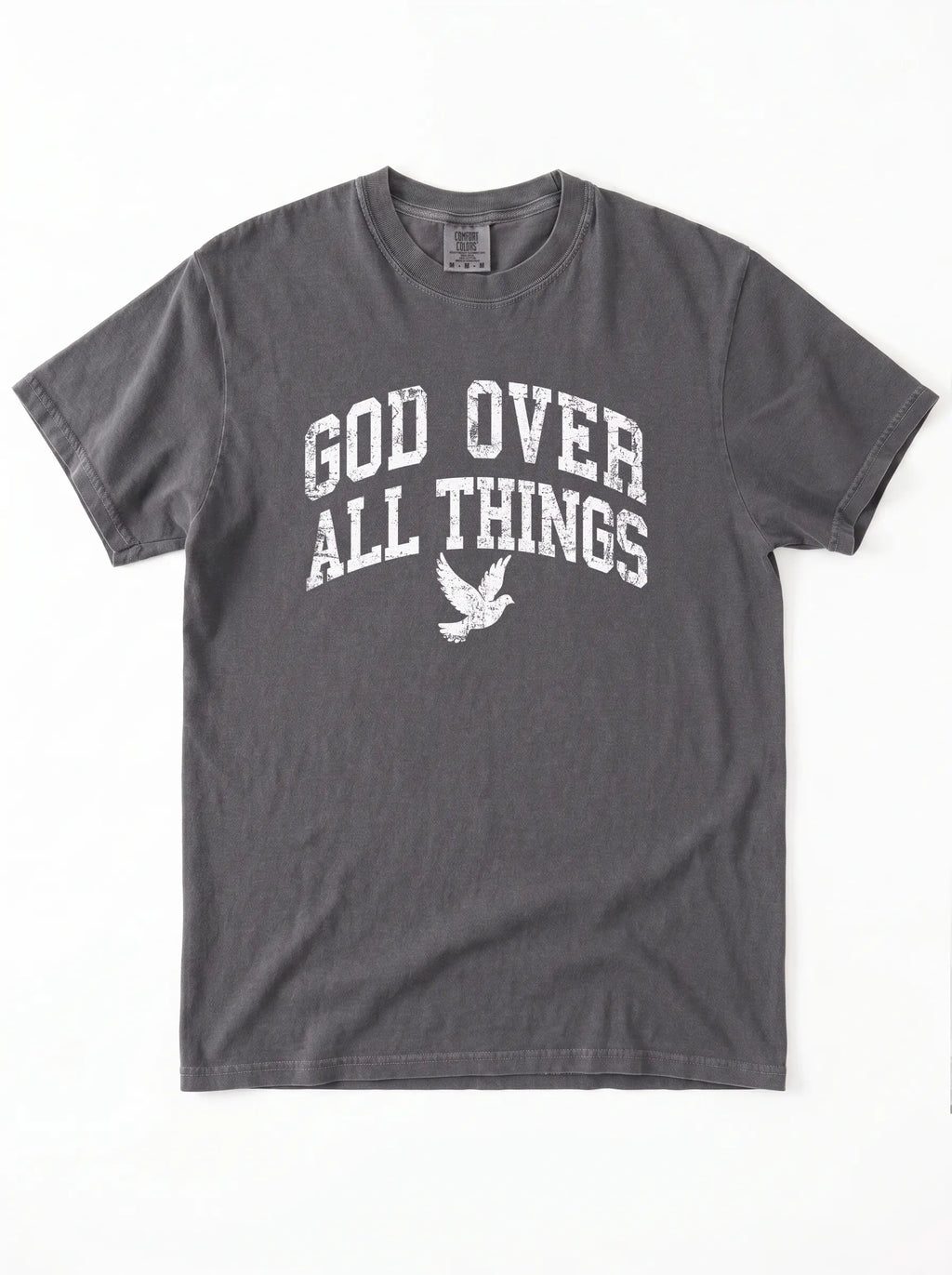 Close-up portrait of a male model looking forward, wearing a charcoal t-shirt featuring a distressed white graphic with the words "GOD OVER ALL THINGS" and a flying dove icon.