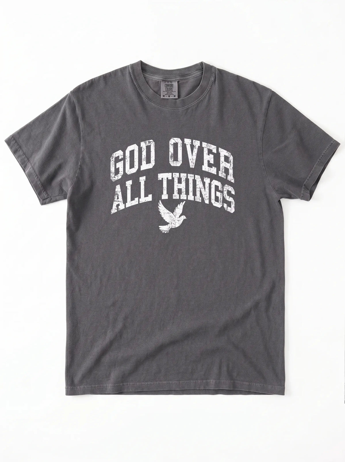 Close-up portrait of a male model looking forward, wearing a charcoal t-shirt featuring a distressed white graphic with the words "GOD OVER ALL THINGS" and a flying dove icon.