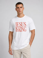 Person wearing a white T-shirt with distressed orange text reading “Jesus Is King.”