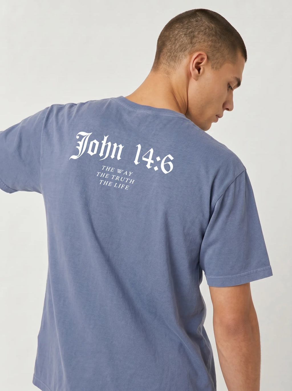 A man wearing a heathered slate blue t-shirt, viewed from the back. The shirt features a white printed graphic on the upper back reading 'John 14:6' in a gothic font, with 'THE WAY THE TRUTH THE LIFE' printed below in a smaller serif font.