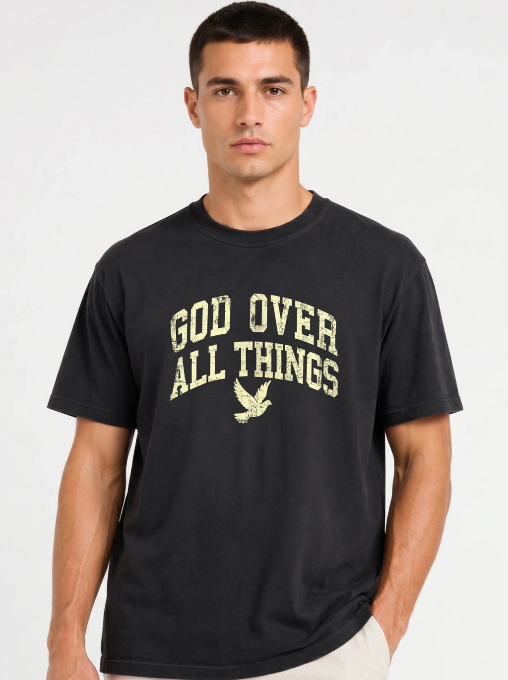 Close-up portrait of a male model wearing a solid black short-sleeve t-shirt with a distressed yellow "GOD OVER ALL THINGS" and dove graphic.