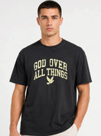 Close-up portrait of a male model wearing a solid black short-sleeve t-shirt with a distressed yellow "GOD OVER ALL THINGS" and dove graphic.