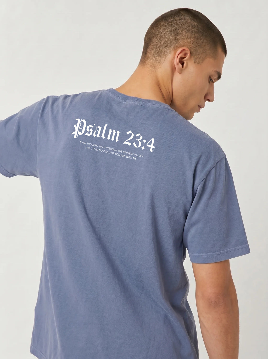 A man wearing a heathered slate blue t-shirt, viewed from behind to show the back graphic which reads 'Psalm 23:4' in a white gothic font with smaller text underneath.