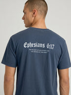A man wearing a navy blue t-shirt, viewed from the back. The shirt features a white gothic-style print of the Bible verse Ephesians 6:17 with additional text below reading 'THE HELMET OF SALVATION AND THE SWORD OF THE SPIRIT'.