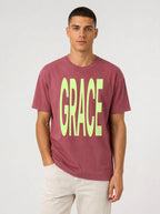 Person wearing a faded red T-shirt with large neon green text reading “GRACE.”