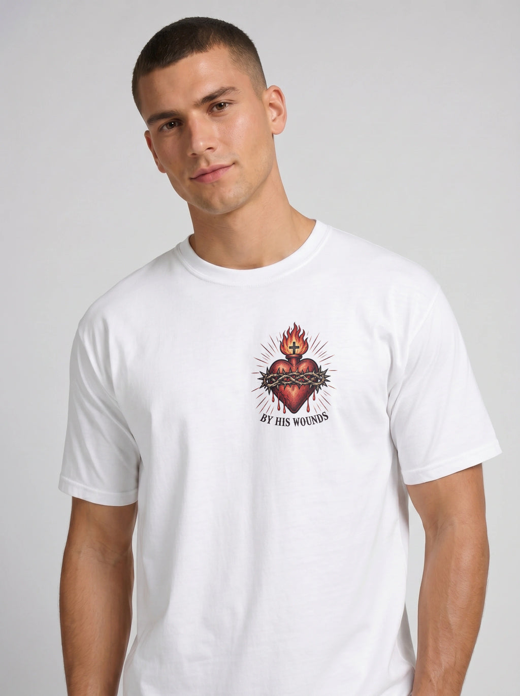 White T-shirt with a flaming sacred heart wrapped in a crown of thorns and the text “By His Wounds.”