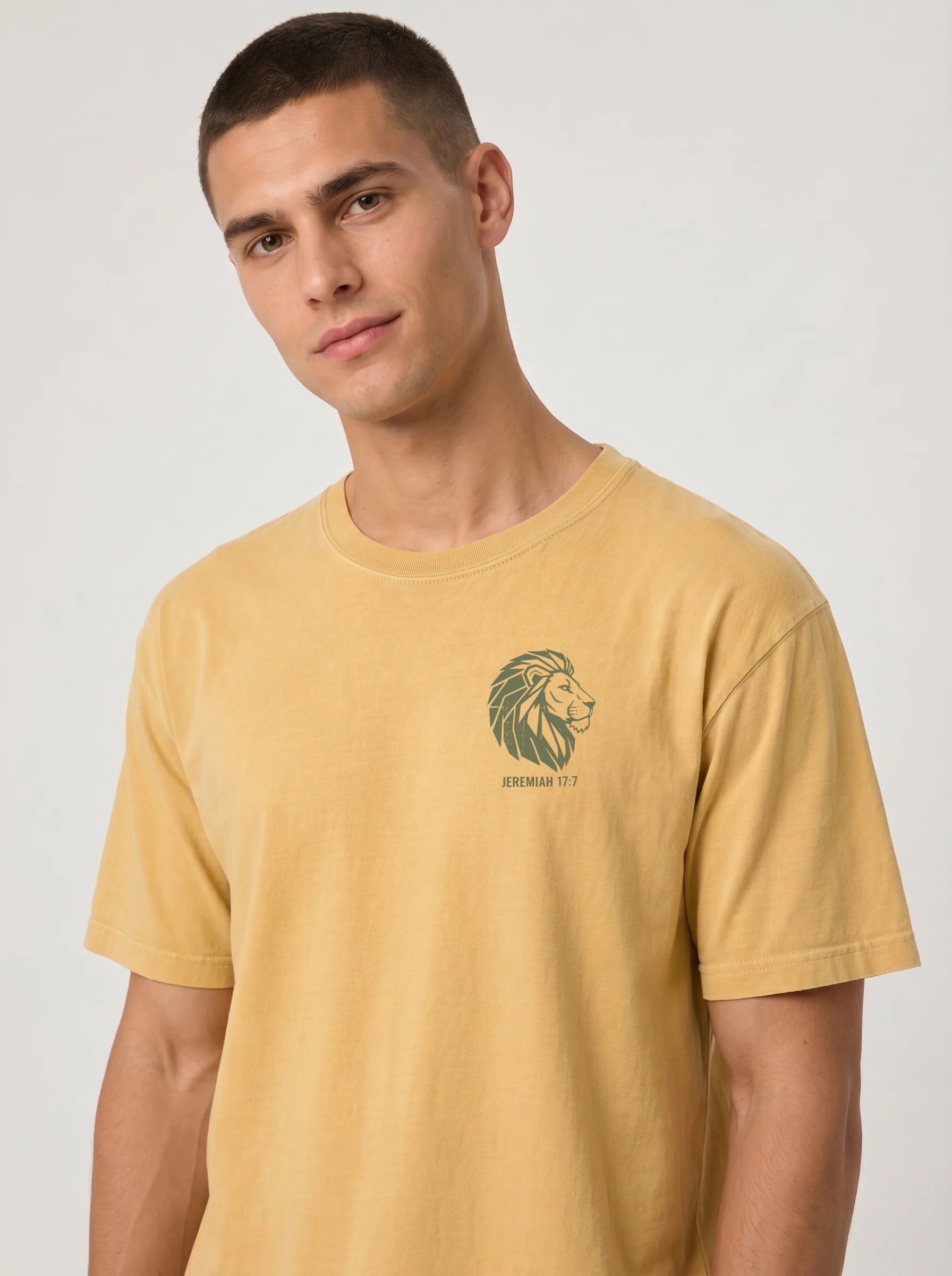 A man wearing a mustard yellow crewneck t-shirt with a green lion graphic and 'JEREMIAH 17:7' text on the left chest, photographed against a light gray studio background.