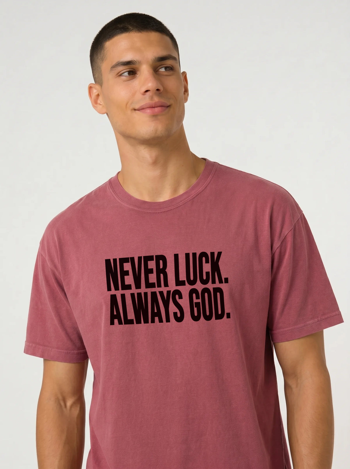 Close-up of a person wearing a faded red T-shirt with black text reading “Never luck. Always God.”