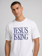 Person wearing a white T-shirt with distressed navy text reading “Jesus Is King.”