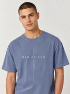 Person wearing a faded blue T-shirt with a cross design and the text “Man of God” and “Romans 8:14.”