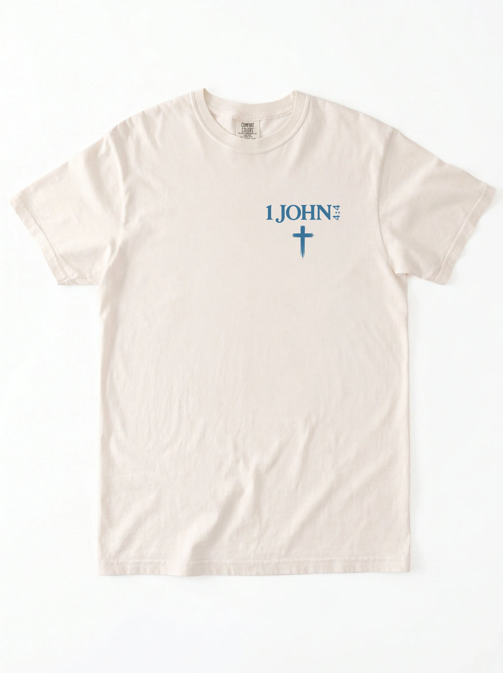 Flat lay of a cream-colored garment-dyed t-shirt, front view, laid on a white surface. It has a small chest print reading '1 JOHN 4:4' with a cross symbol beneath it.