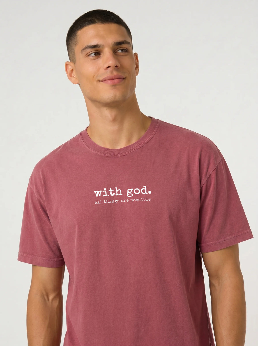 A man wearing a heathered dusty rose t-shirt with the white printed text 'with god. all things are possible' on the chest, photographed against a light gray studio background.