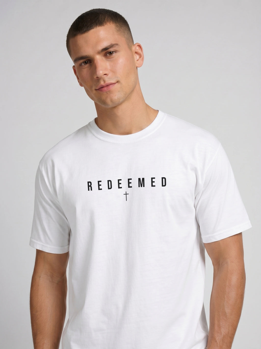 A man wearing a white crew-neck t-shirt with the word 'REDEEMED' and a cross printed on the chest, set against a plain light gray background.