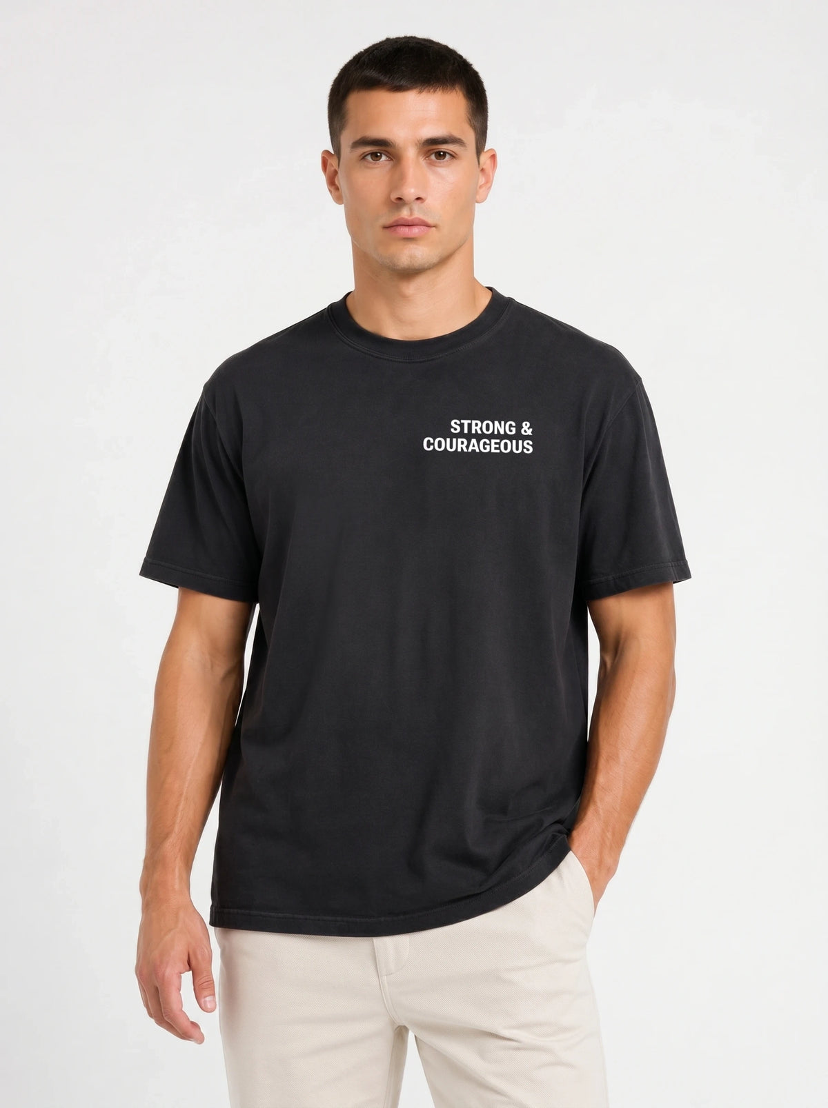 Person wearing a black T-shirt with small white chest text reading “Strong & courageous.”