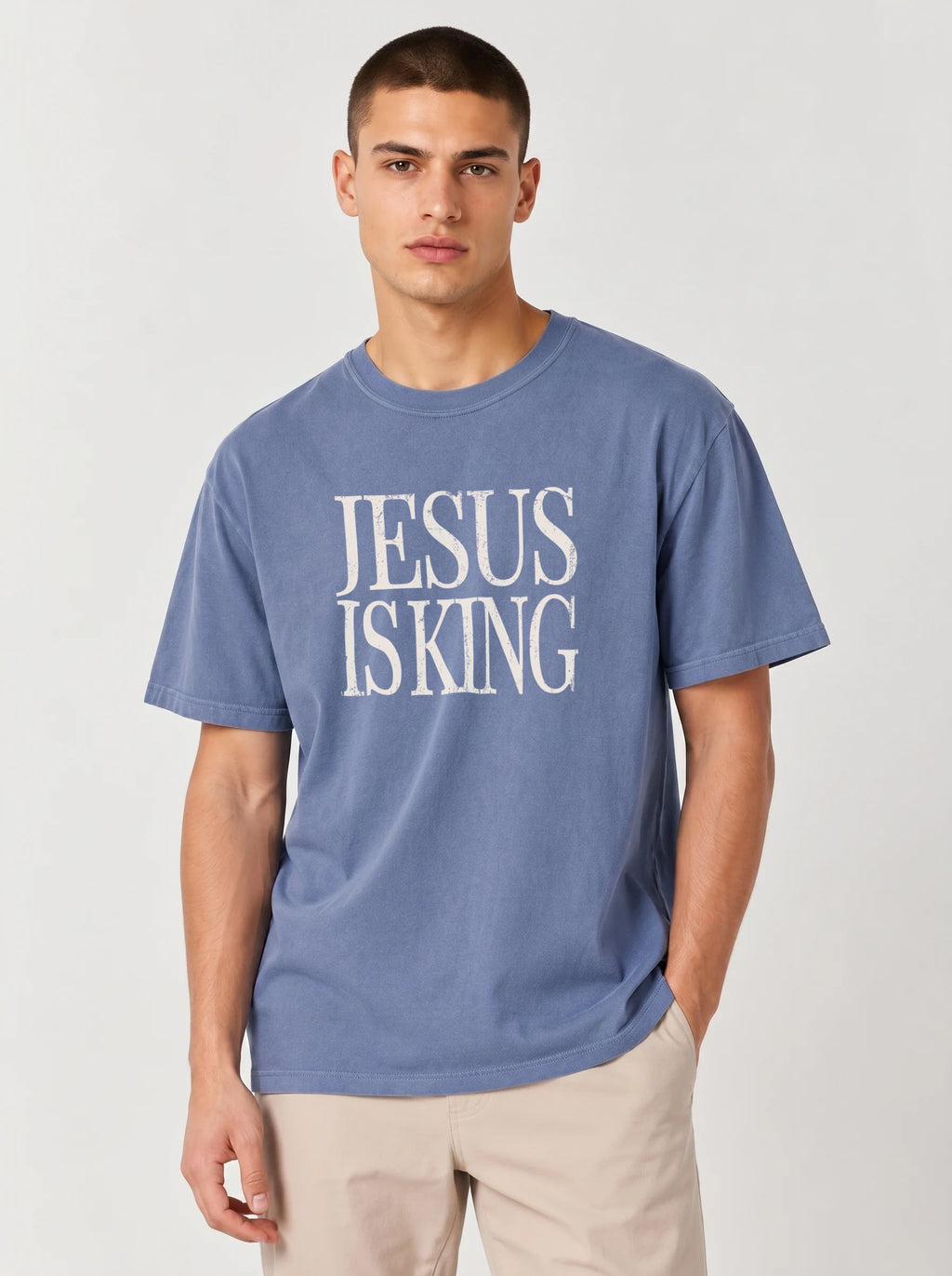 Person wearing a muted blue T-shirt with distressed cream text reading “Jesus Is King.”